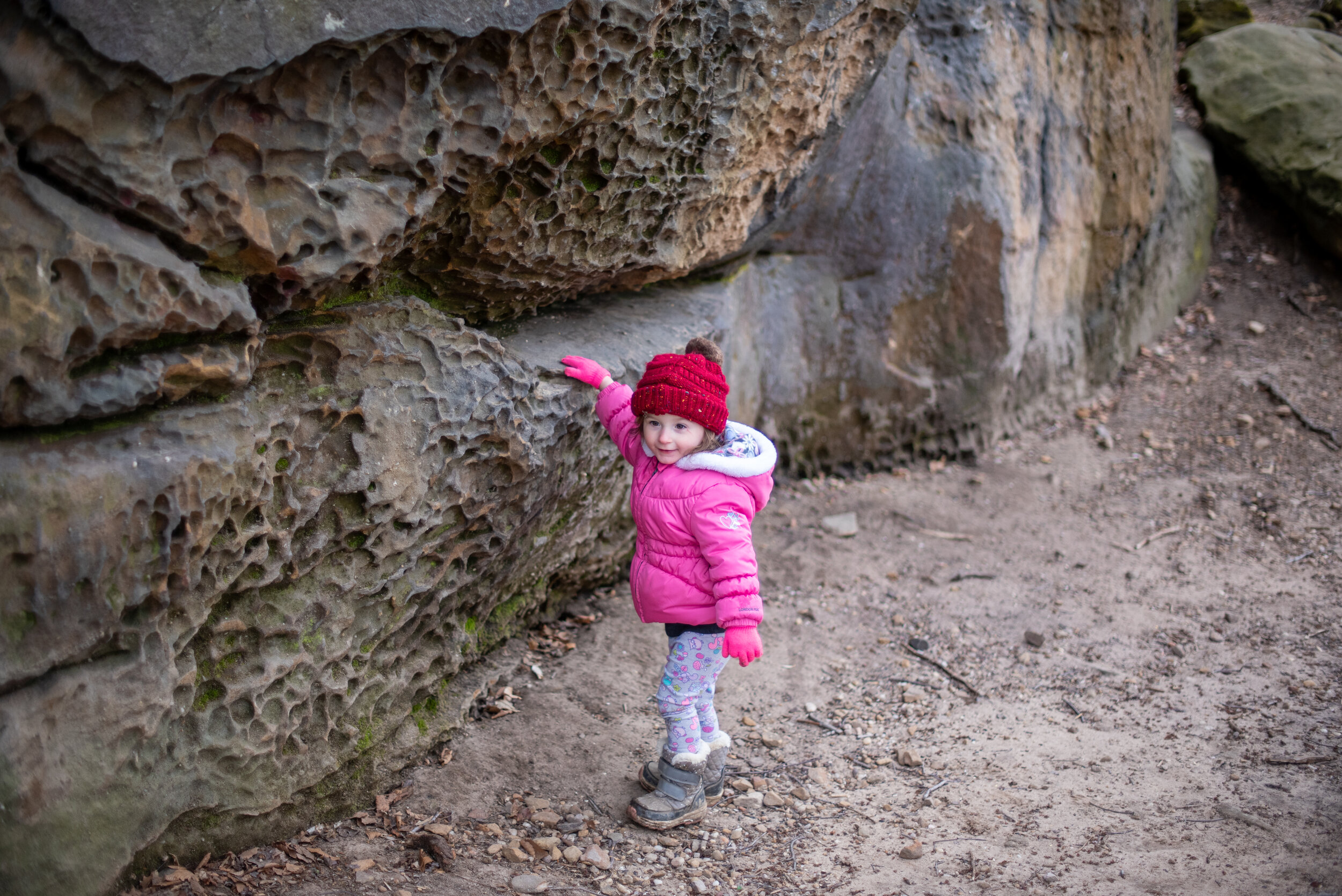 little girl dresses in winter gear touching a large rock wall in cleveland ohio