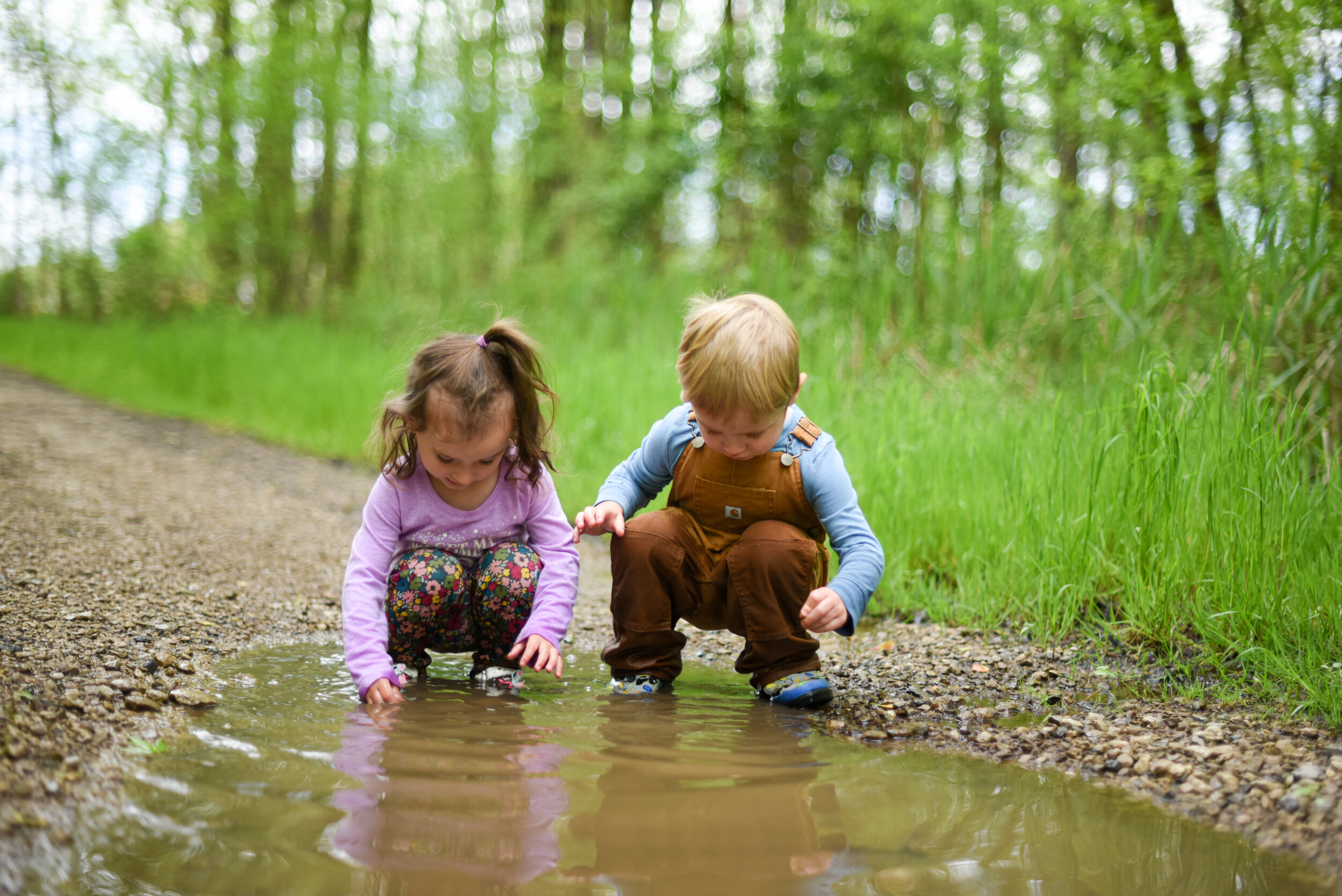 little girl and little boy playing outside in a puddle