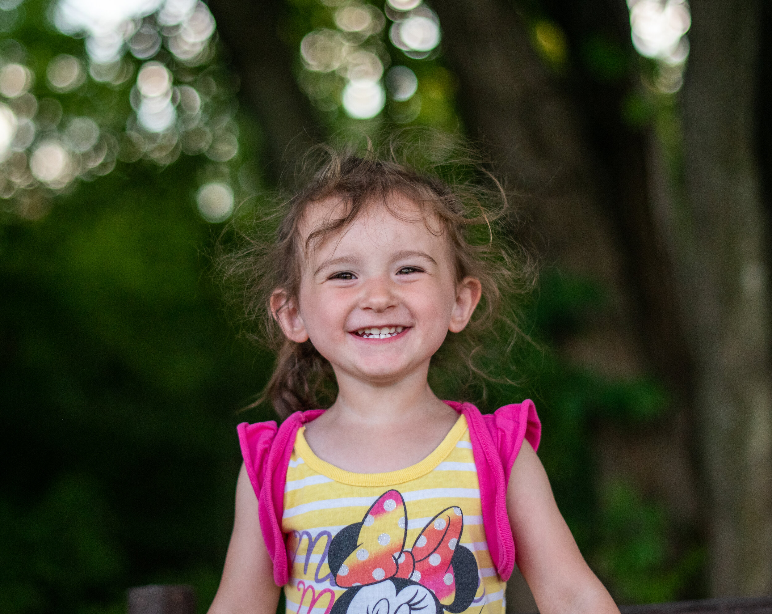 little girl in pink and yellow striped mini mouse shirt smiling at the camera with wild hair