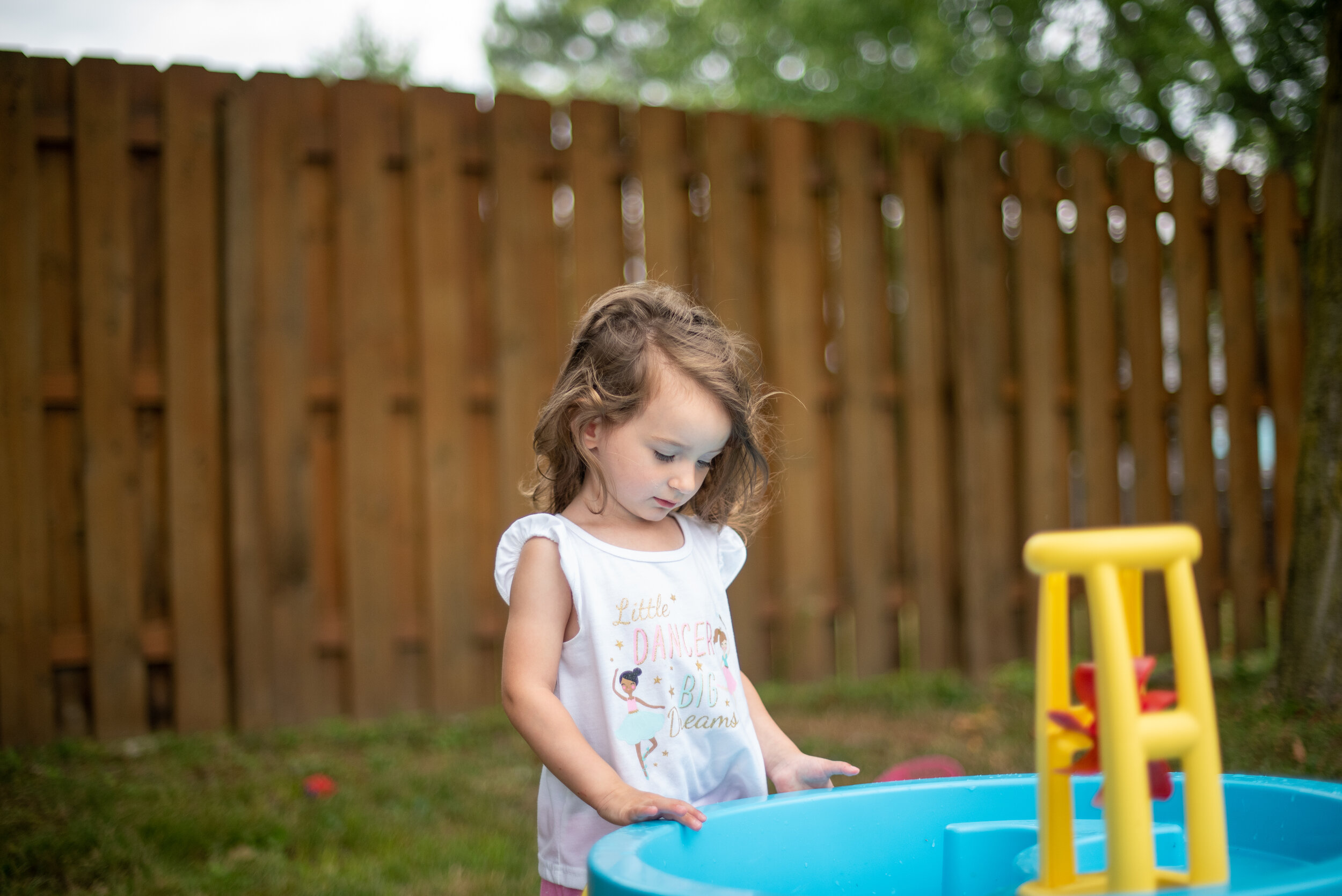 little girl outside looking at the water in a blue water table during a summer morning in northeast ohio