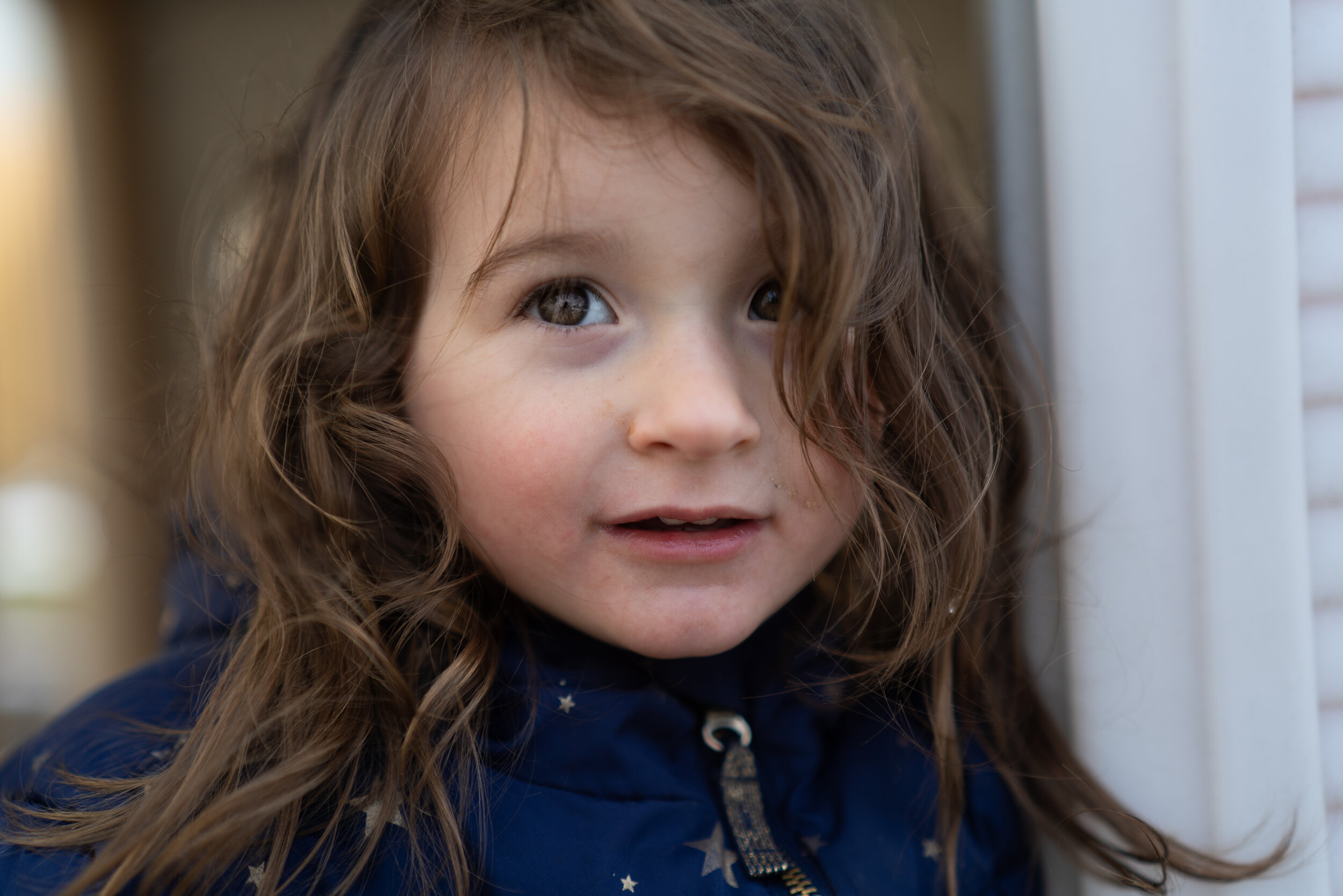 portrait of a little girl with brown hair and grey eyes in a blue jacket with gold stars looking off into the distance