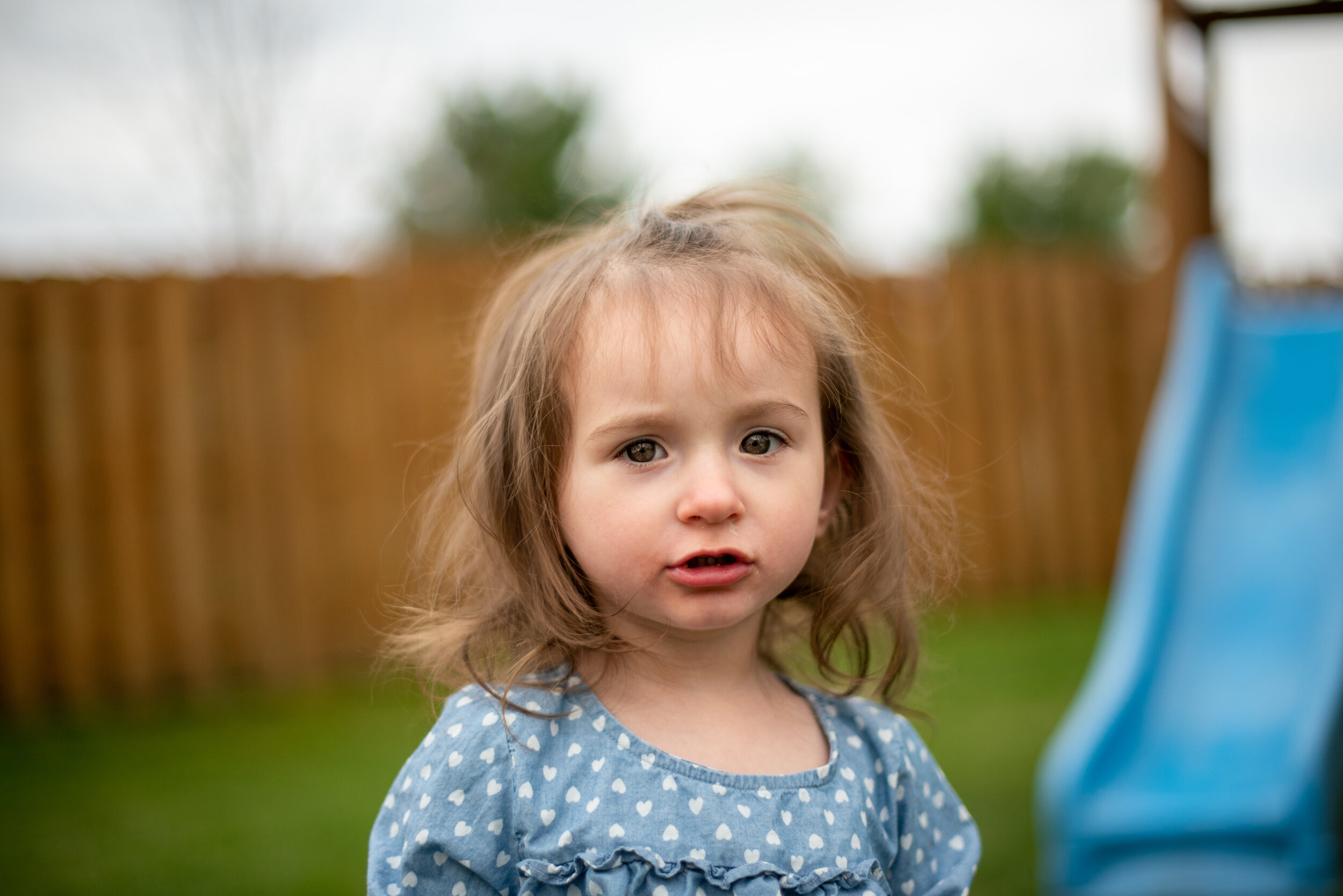 little girl outside in polka dot dress and messy hair looking at camera