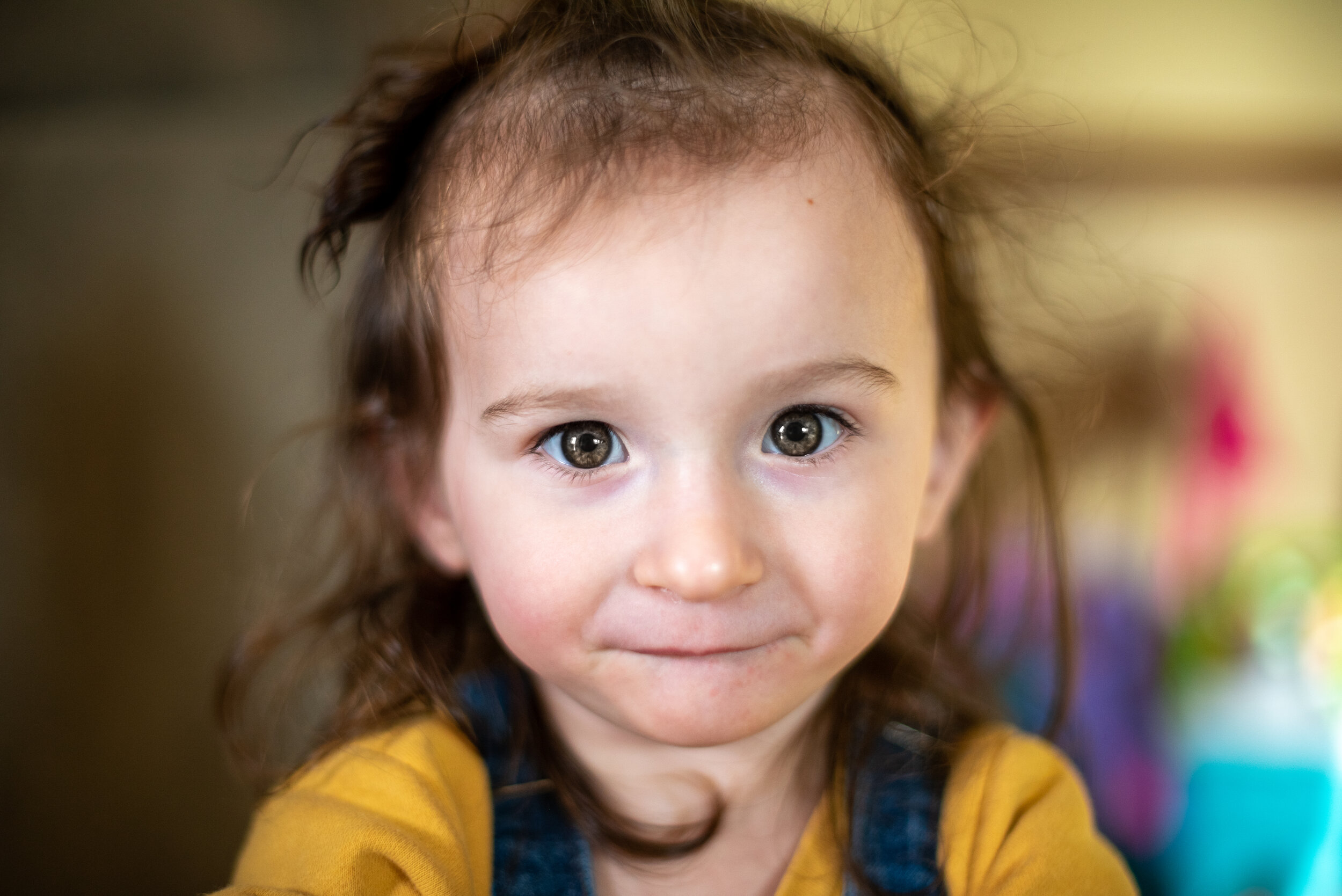 little girl with grey eyes and brown hair wearing a yellow shirt looking at camera