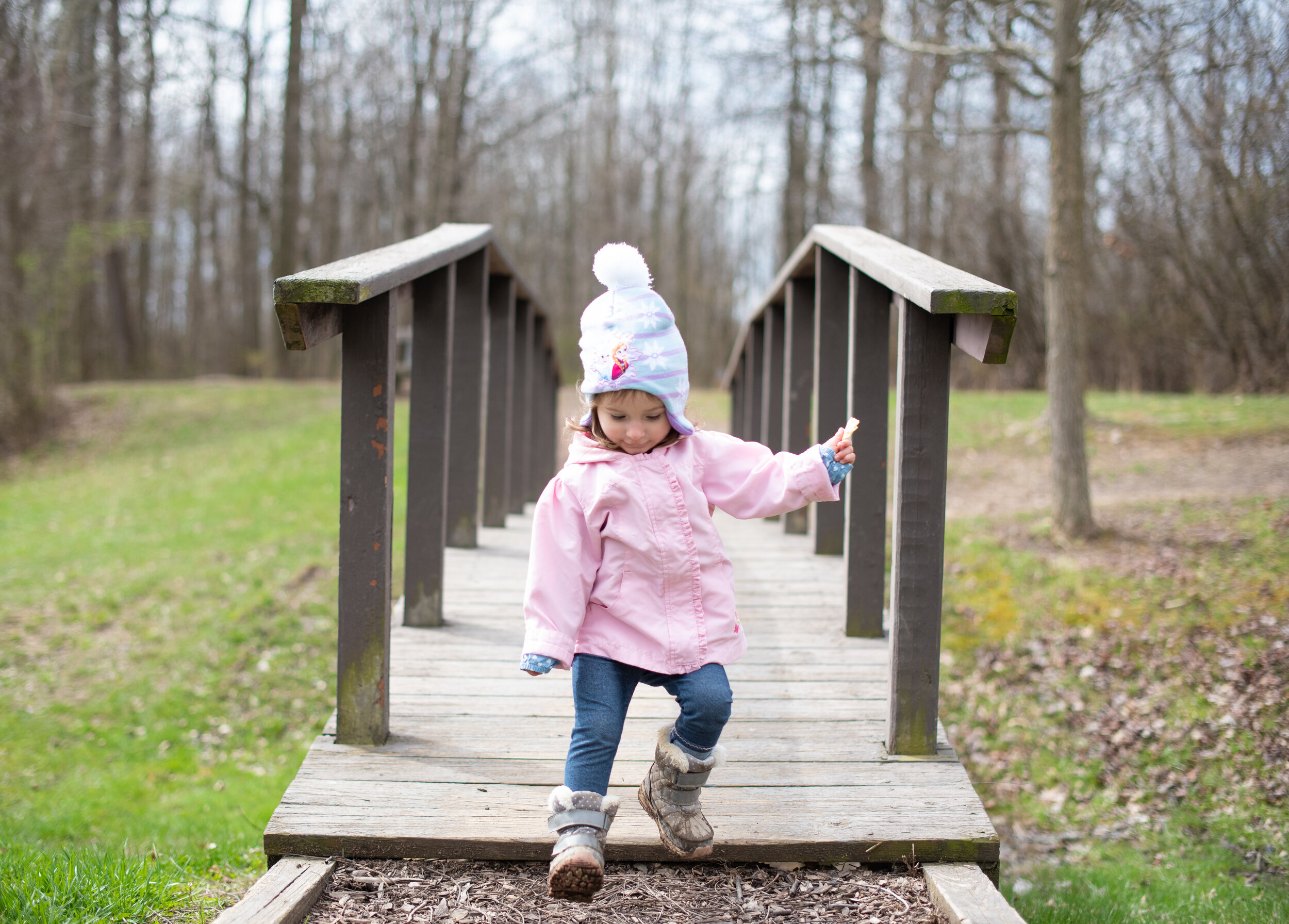 girl in blue hat and pink jacket running off a small bridge outdoors in the winter 