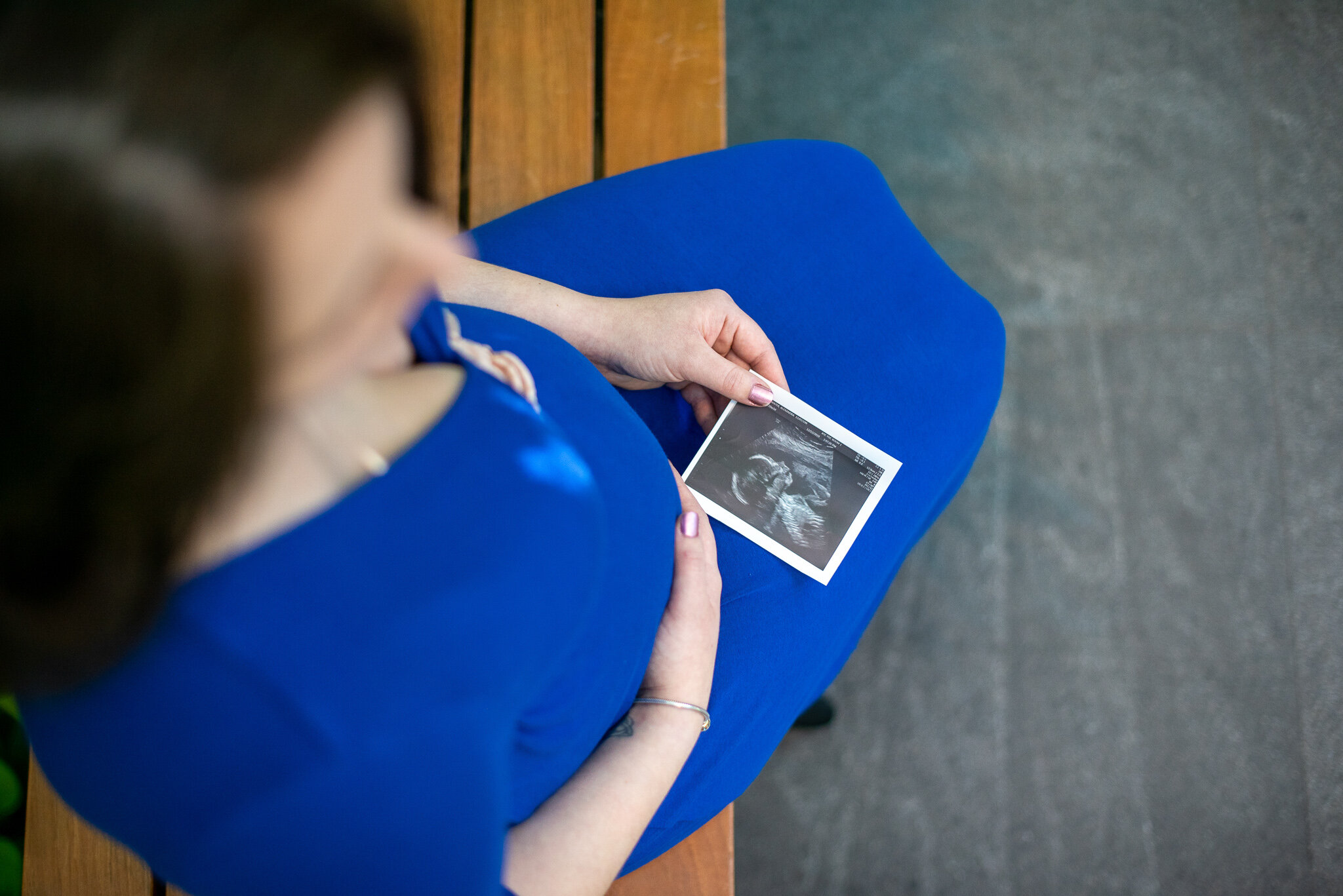pregnant mother sitting on a bench holding her belly and holding a sonogram in the other hand in cleveland ohio
