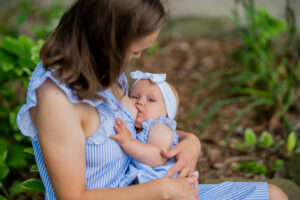 baby and mom in matching blue dresses snuggled together while baby breastfeeds 