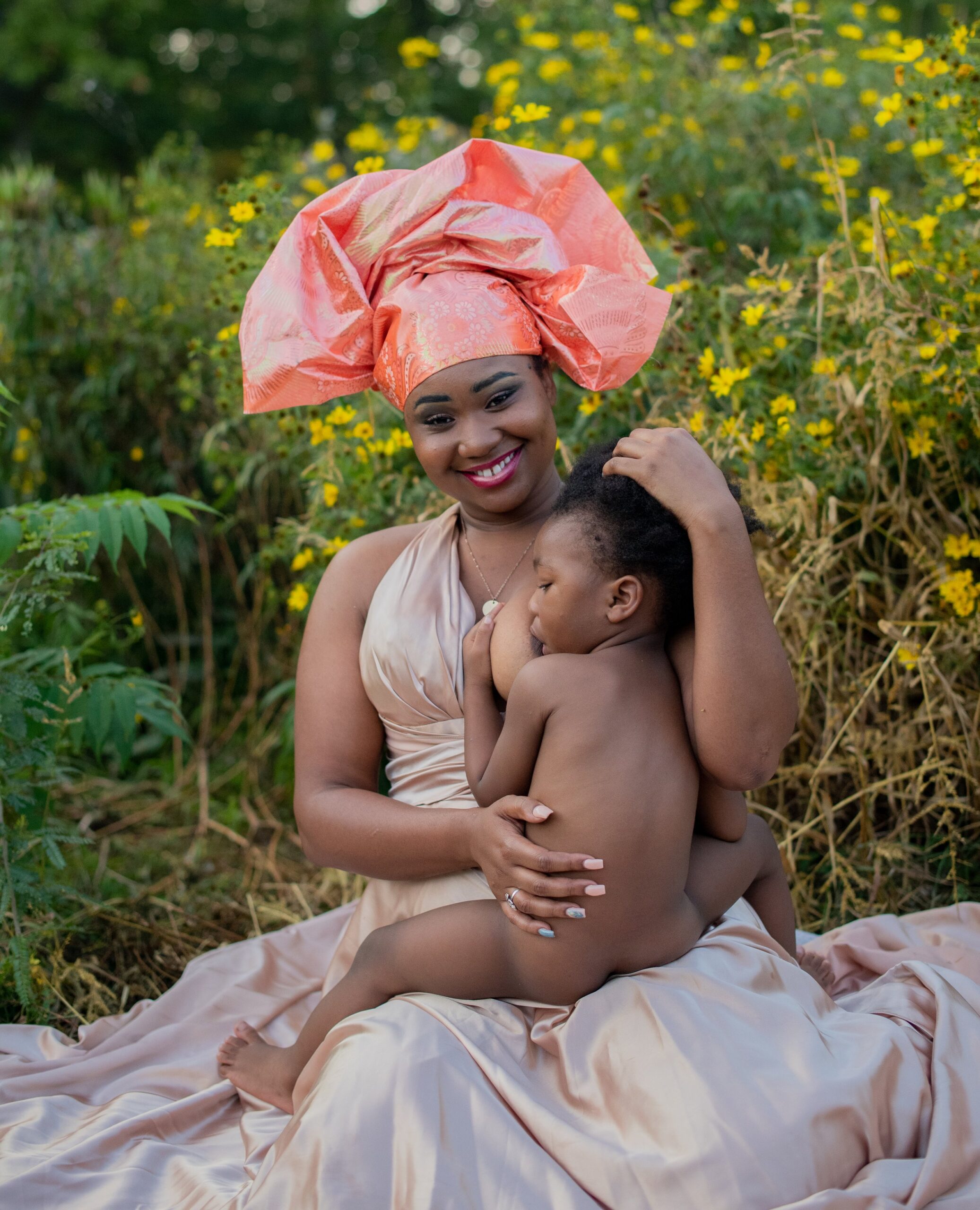 African American mother holding her son while breastfeeding outside in a yellow flower field 