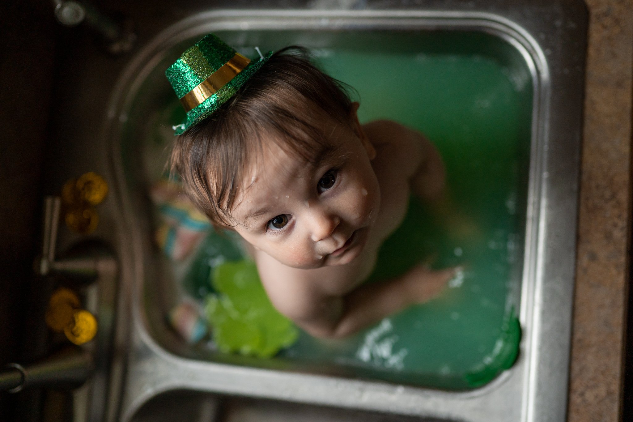 little boy in st patrick's day attire staring up at camera while sitting in green water 