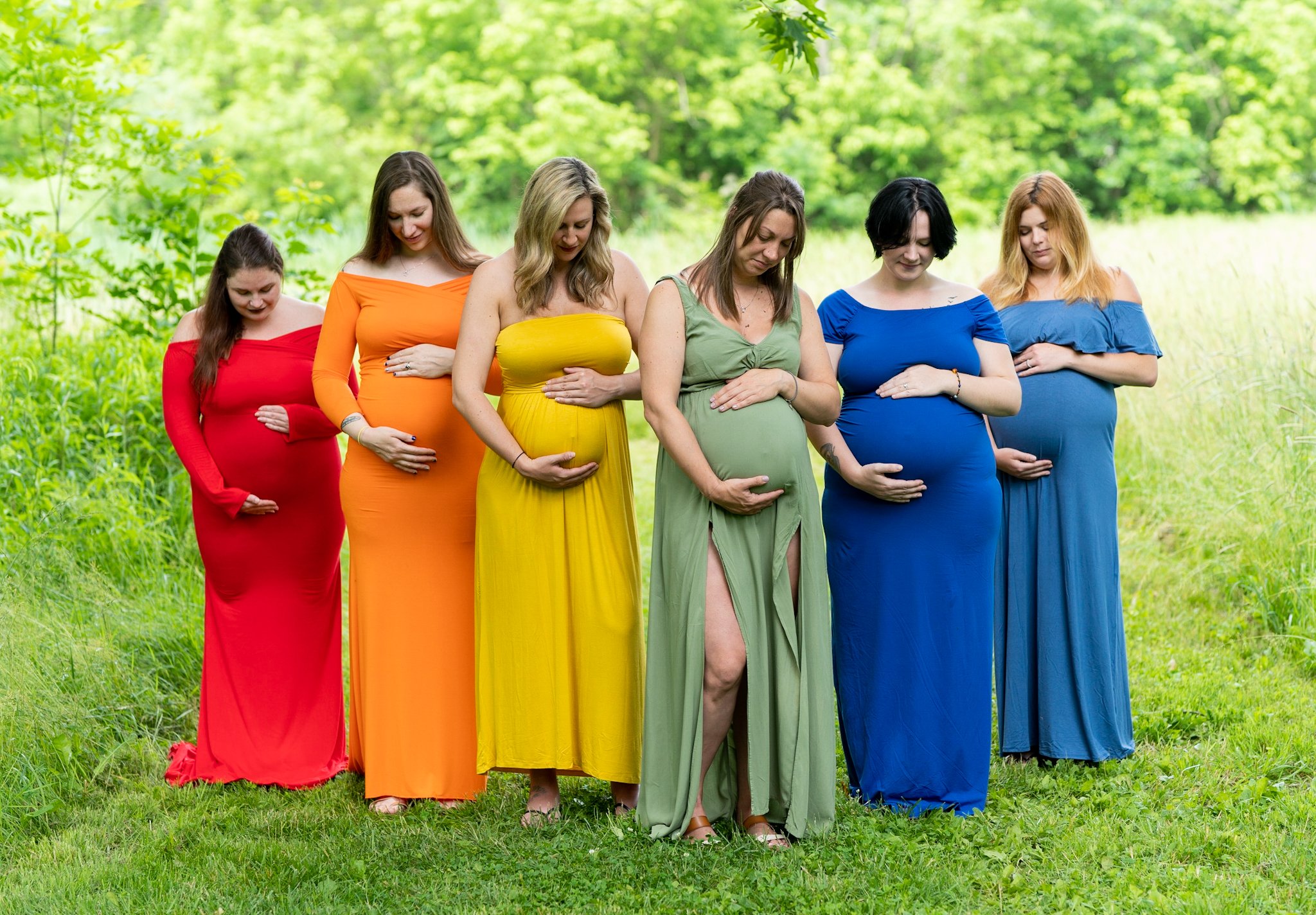 pregnant mothers holding their baby bumps and looking down at them in dress colors that make the rainbow at paw paw picnic area 