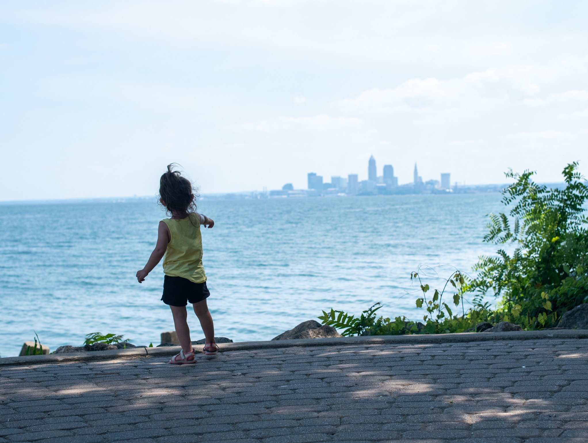little girl pointing to Cleveland skyline across the water on a summer day at Lakewood park