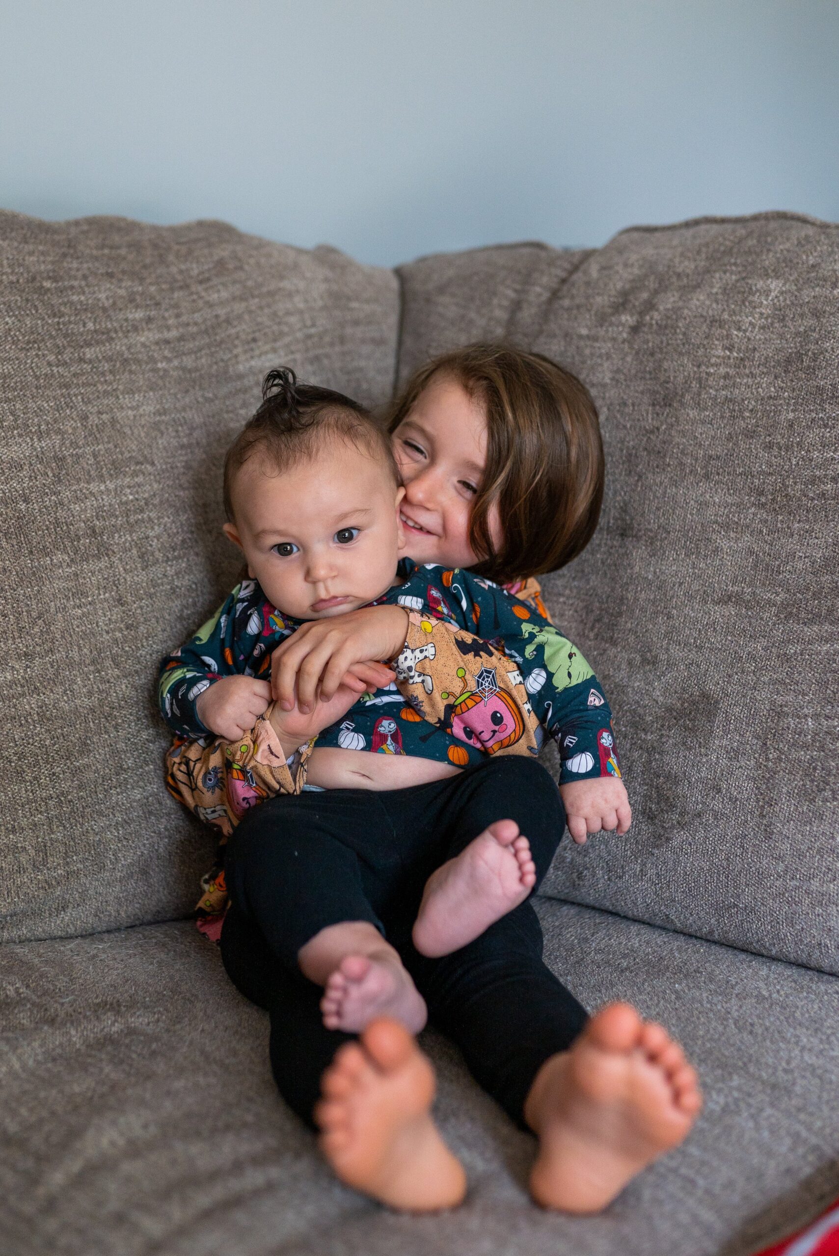 little girl hugging her brother on the couch while brother looks the other way