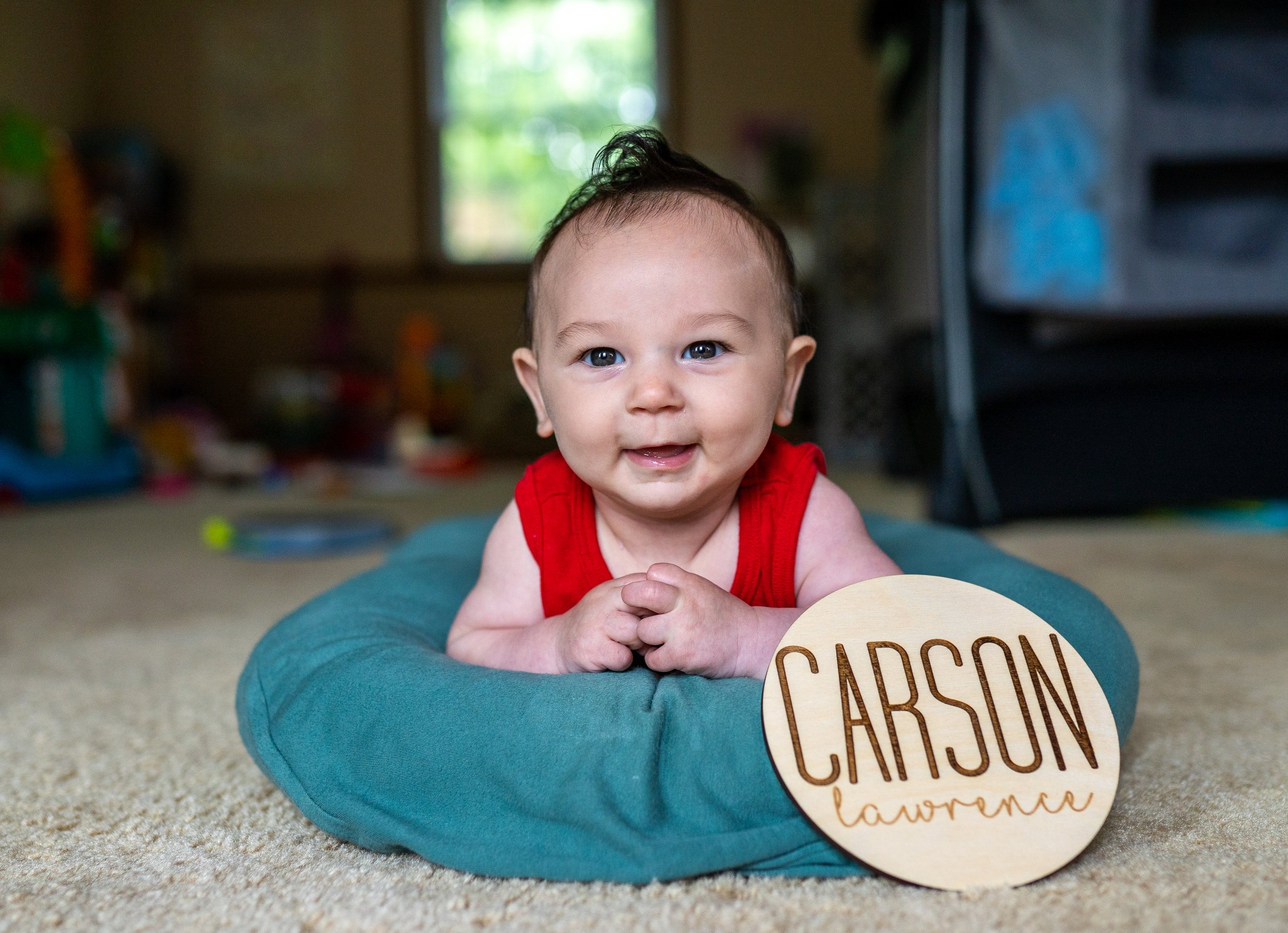 little boy on pillow looking at the camera with a sign that says carson lawrence next to him Happy 1st Birthday Boy