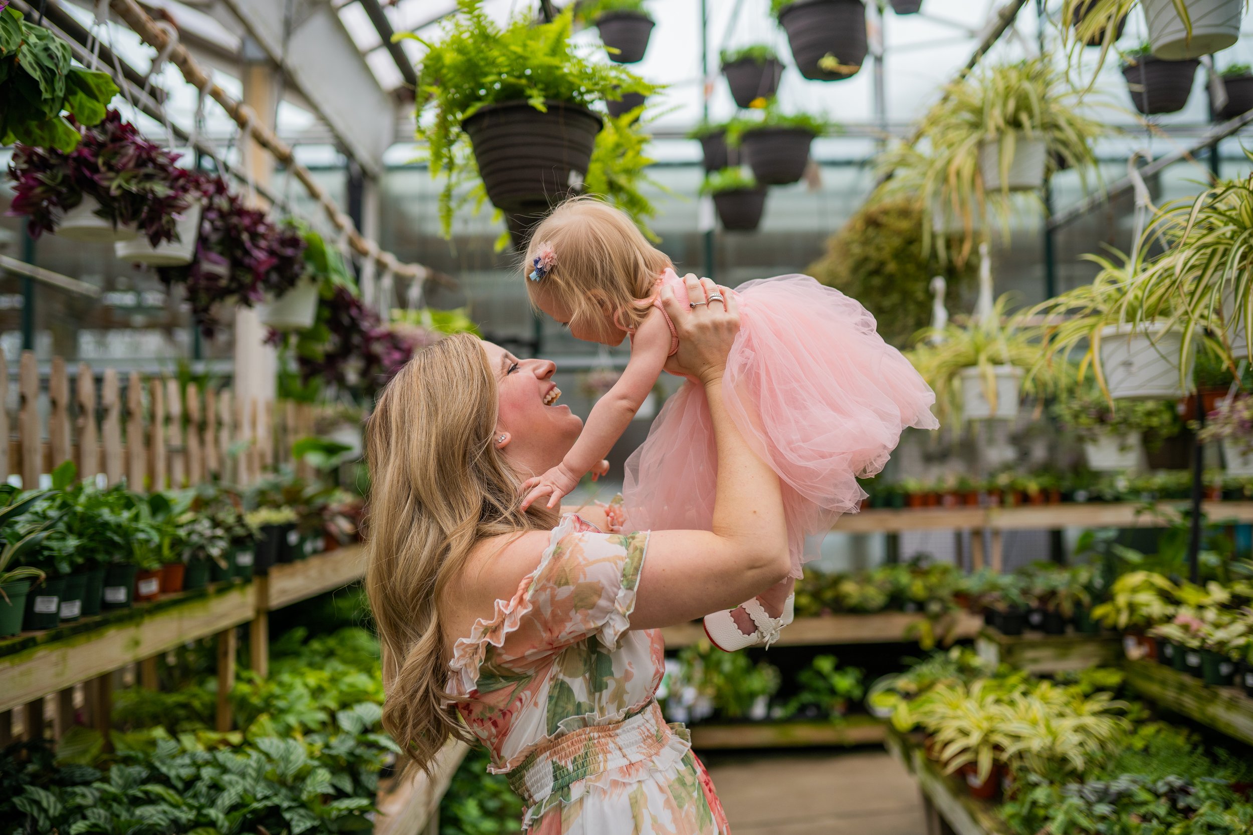 mother holding up baby girl in greenhouse