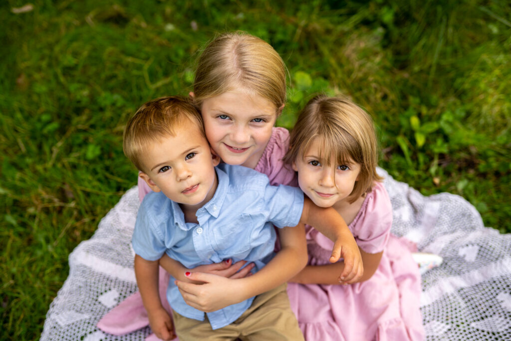 two sisters and brother cuddle and smile at the camera