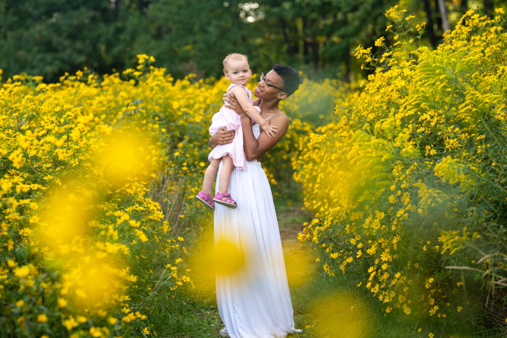 Mother holding her daughter while smiling at her in a field of yellow flowers in huntington beach ohio