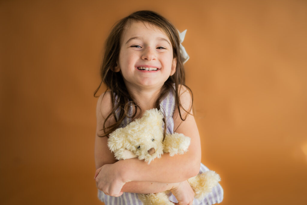 little girl smiling at camera and hugging a stuffed animal bear