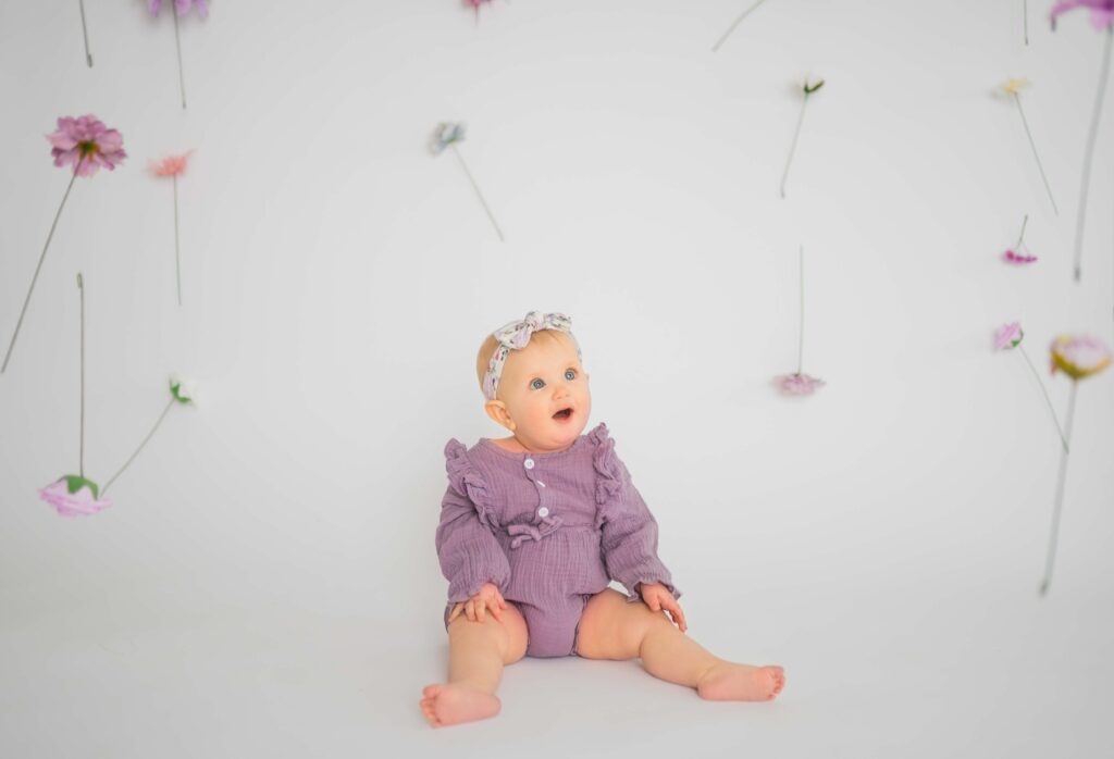 little girl in a lilac onsie with floating flowers surrounding her as she looks in awe at a flower