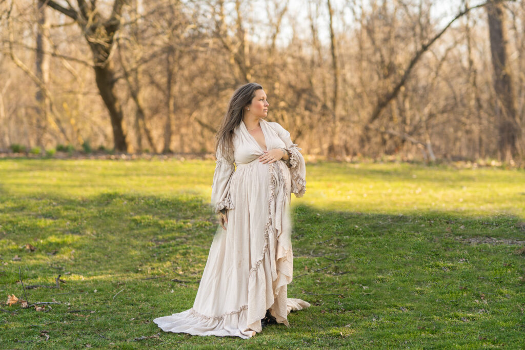 pregnant mama bird looking off into the distance with one hand on her belly in a beige maternity gown