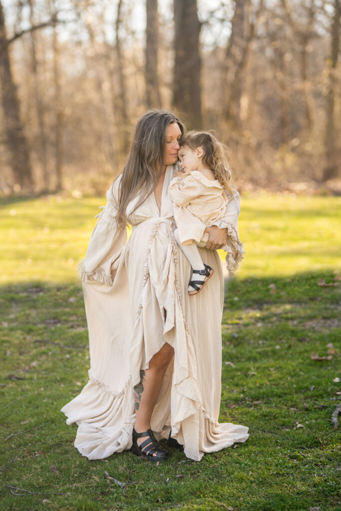 mother holding her toddler and cuddling while moving her beige maternity gown 