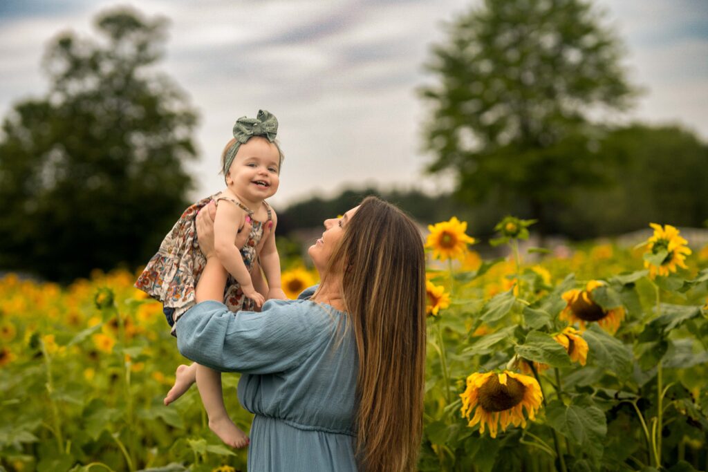 mom holding up her daughter in a field of sunflowers 